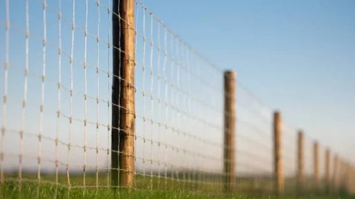 a fence line of some farm land featuring agricultural fencing and wire